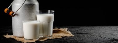 Rustic milk in a can and a glass on the table. On a black background. High quality photo