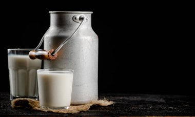 Rustic milk in a can and a glass on the table. On a black background. High quality photo