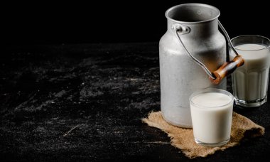 Rustic milk in a can and a glass on the table. On a black background. High quality photo
