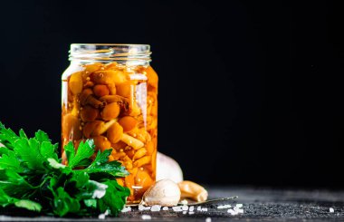 A glass jar with marinated mushrooms on the table. On a black background. High quality photo