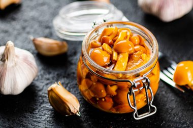 Marinated mushrooms in a glass jar with cloves of garlic. On a black background. High quality photo