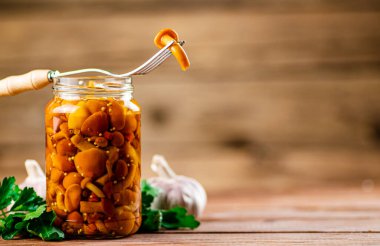 Glass jar with marinated mushrooms. On a wooden background. High quality photo