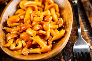 Marinated mushrooms on a wooden plate. On a rustic dark background. High quality photo