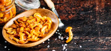 Marinated mushrooms on a wooden plate. On a rustic dark background. High quality photo