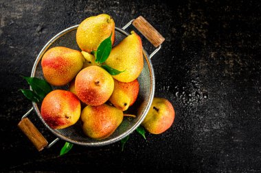 Juicy pears in a colander with foliage. On a black background. High quality photo