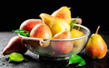 Fresh pears with leaves in a colander. On a black background. High quality photo