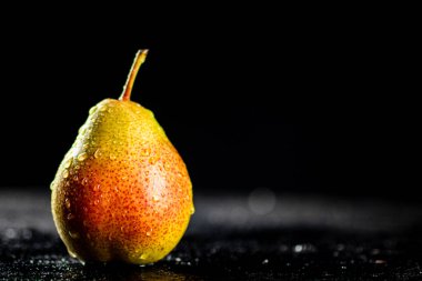 One pear with drops of water on the table. On a black background. High quality photo