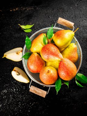 Fresh pears with leaves in a colander. On a black background. High quality photo