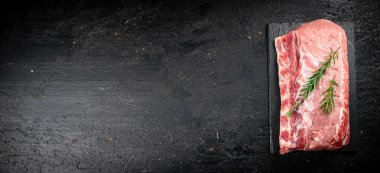 A piece of raw pork on a stone board with a sprig of rosemary. On a black background. High quality photo