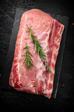 A piece of raw pork on a stone board with a sprig of rosemary. On a black background. High quality photo