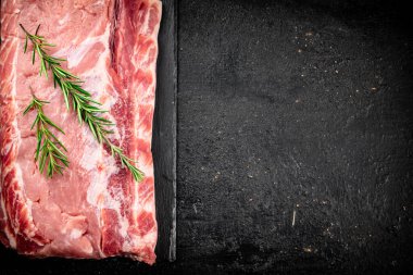 A piece of raw pork on a stone board with a sprig of rosemary. On a black background. High quality photo
