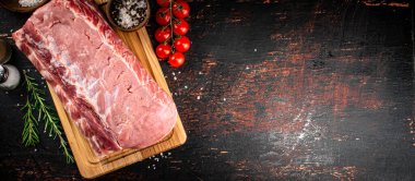 A piece of raw pork on a cutting board with tomatoes, spices and rosemary. On a rustic dark background. High quality photo