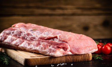 Raw pork on a cutting board with fresh tomatoes. On a wooden background. High quality photo