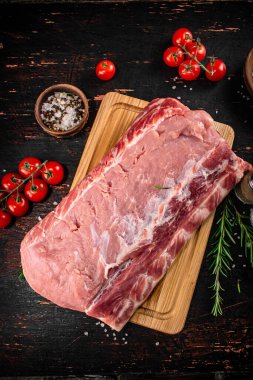 A piece of raw pork on a cutting board with tomatoes, spices and rosemary. On a rustic dark background. High quality photo