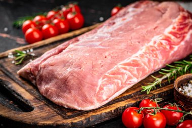 A piece of raw pork on a cutting board with tomatoes, spices and rosemary. On a rustic dark background. High quality photo