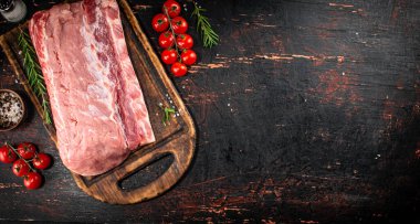 A piece of raw pork on a cutting board with tomatoes, spices and rosemary. On a rustic dark background. High quality photo