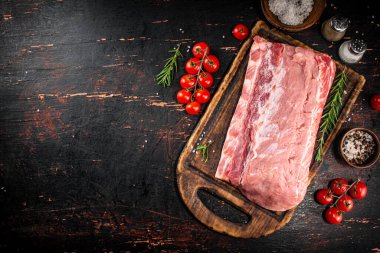 A piece of raw pork on a cutting board with tomatoes, spices and rosemary. On a rustic dark background. High quality photo