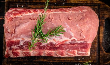 A piece of raw pork on a cutting board with a sprig of rosemary. On a rustic dark background. High quality photo
