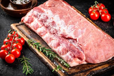 Raw pork on a cutting board with tomatoes, rosemary and spices. On a black background. High quality photo