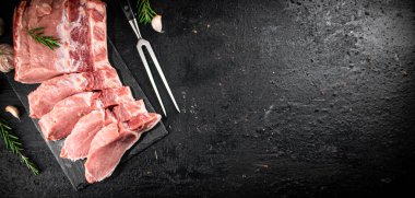 Chopped raw pork on a stone board with rosemary and garlic. On a black background. High quality photo