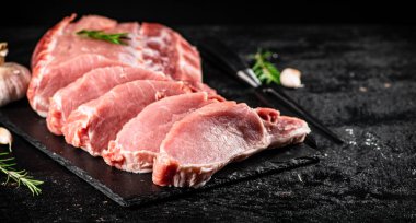 Chopped raw pork on a stone board with rosemary and garlic. On a black background. High quality photo