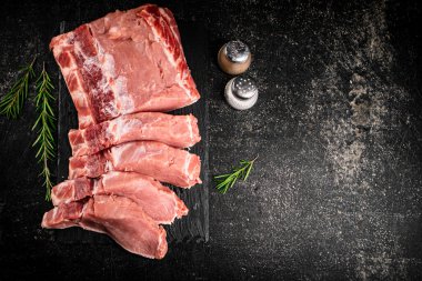 Pieces of raw pork on a stone board with rosemary and spices. On a black background. High quality photo