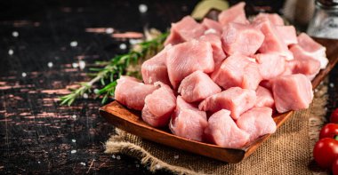 Pieces of raw pork on a wooden plate with a sprig of rosemary. Against a dark background. High quality photo