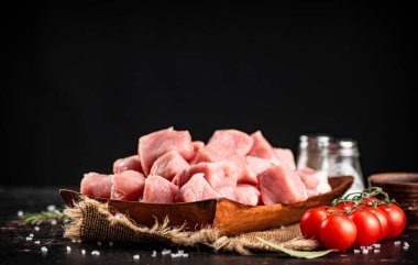 Pieces of raw pork on a wooden plate with spices and tomatoes. On a black background. High quality photo