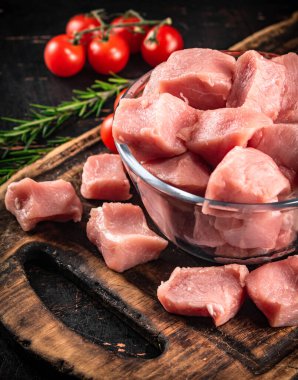 Pieces of raw pork in a glass bowl with tomatoes and rosemary. Against a dark background. High quality photo