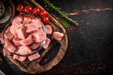 Pieces of raw pork in a glass bowl with tomatoes and rosemary. Against a dark background. High quality photo