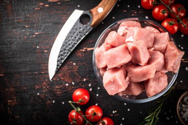 Pieces of raw pork in a glass bowl with tomatoes and rosemary. Against a dark background. High quality photo