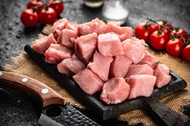 Pieces of raw pork on a cutting board with tomatoes. On a black background. High quality photo