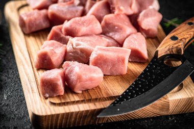 Pieces of raw pork on a wooden cutting board with a knife. On a black background. High quality photo