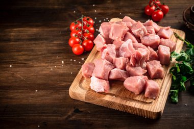 Pieces of raw pork on a cutting board with parsley and tomatoes. On a wooden background. High quality photo