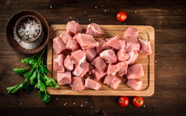 Pieces of raw pork on a cutting board with parsley and tomatoes. On a wooden background. High quality photo