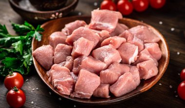 Raw pork sliced on a plate with tomatoes. On a wooden background. High quality photo