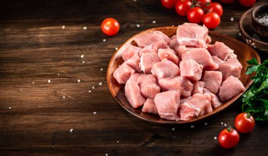 Raw pork sliced on a plate with tomatoes. On a wooden background. High quality photo