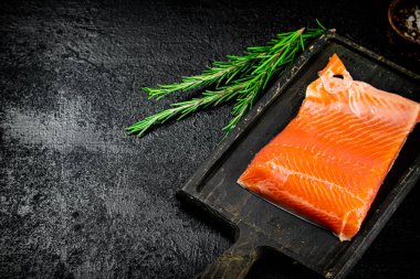 Salted salmon on a cutting board with rosemary. On a black background. High quality photo