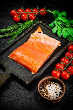 Salted salmon with greens and tomatoes on a cutting board. On a black background. High quality photo