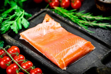 Salted salmon with greens and tomatoes on a cutting board. On a black background. High quality photo