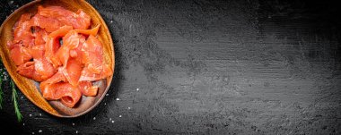 A wooden plate with slices of salted salmon. On a black background. High quality photo