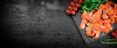 Salted salmon on a stone board with tomatoes and greens. On a black background. High quality photo
