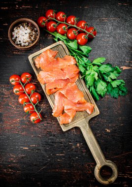 Slices of salted salmon with greens and tomatoes on a cutting board. Against a dark background. High quality photo