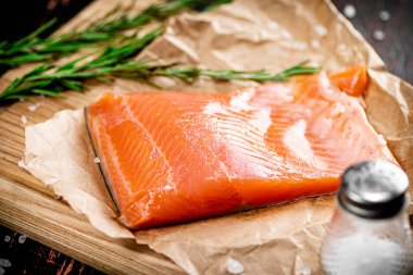 A piece of salted salmon on a cutting board with rosemary and spices. Against a dark background. High quality photo