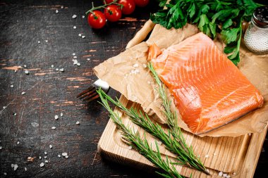 A piece of salted salmon on a cutting board with rosemary and spices. Against a dark background. High quality photo