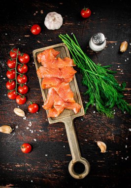 Slices of salted salmon on a cutting board with dill and tomatoes. Against a dark background. High quality photo