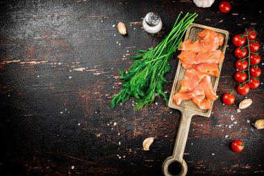 Slices of salted salmon on a cutting board with dill and tomatoes. Against a dark background. High quality photo