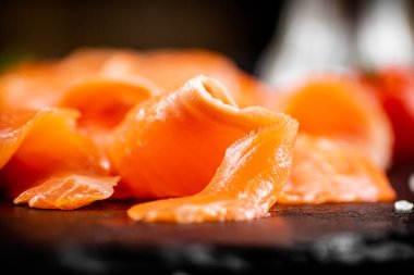 Pieces of salted salmon with greenery on a stone board. On a black background. High quality photo