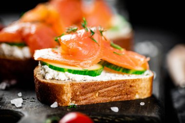 Sandwich with pieces of salmon on a cutting board. On a black background. High quality photo
