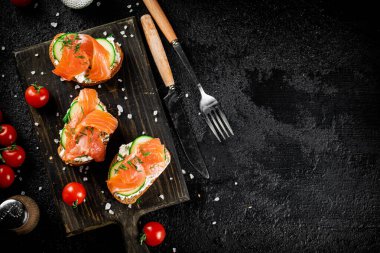 Sandwich with pieces of salmon on a cutting board. On a black background. High quality photo